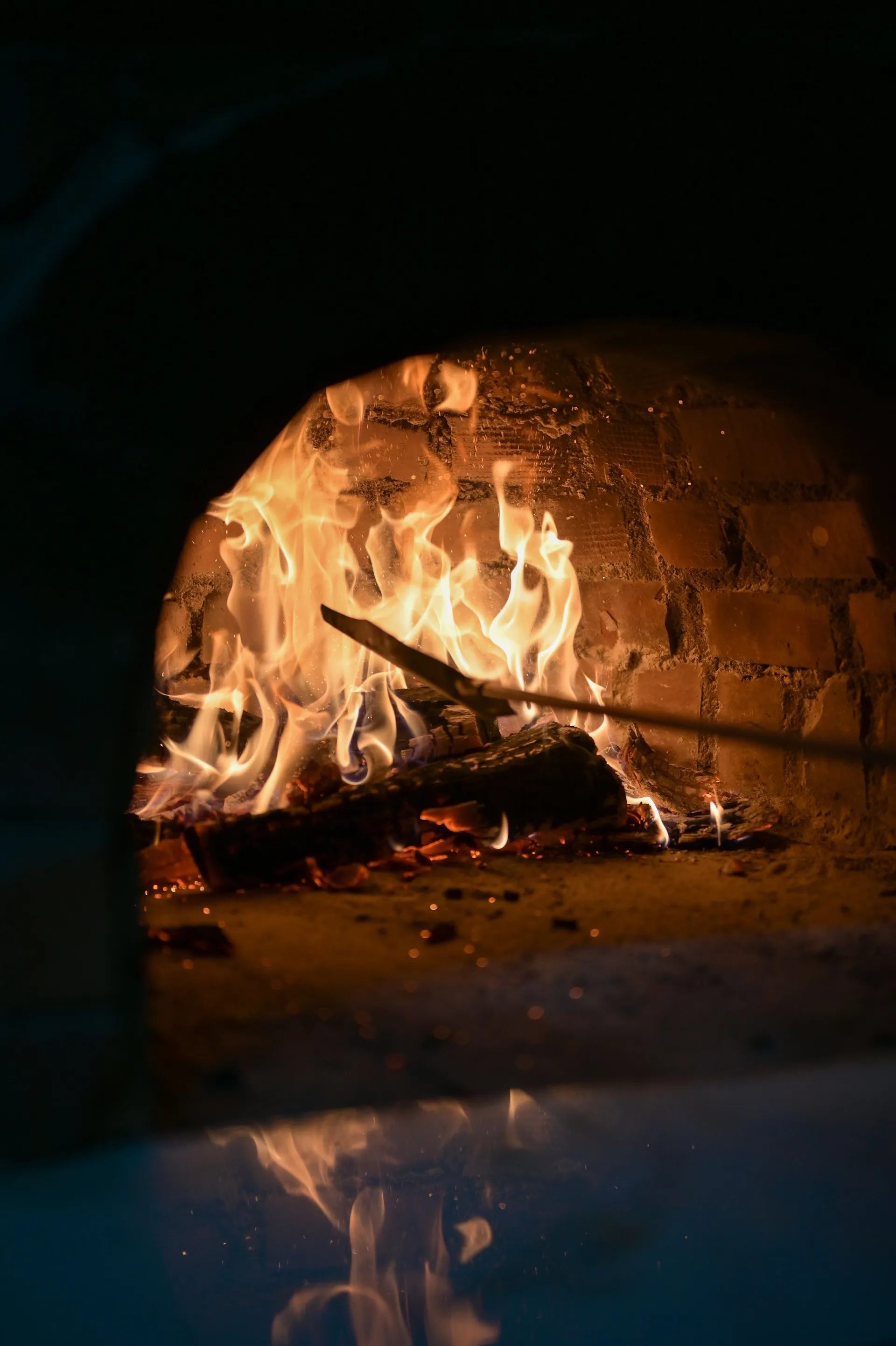 Boca de forno a lenha aceso à noite, chamas e brasas iluminando o escuro